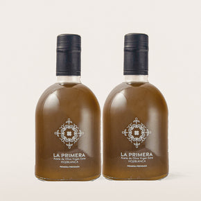 Two transparent bottles labeled "LA PRIMERA' Premium Extra Virgin Olive Oil 'Hojiblanca varietal' with Spanish tile logo. 